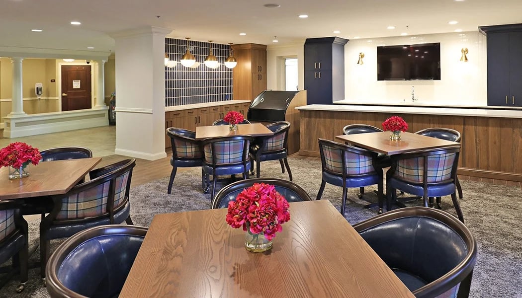 A modern dining area with wooden tables and chairs, decorated with red flowers.