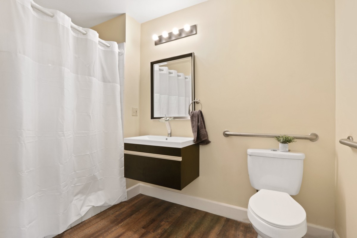 A modern bathroom featuring a floating sink, large mirror, and a shower with a white curtain.
