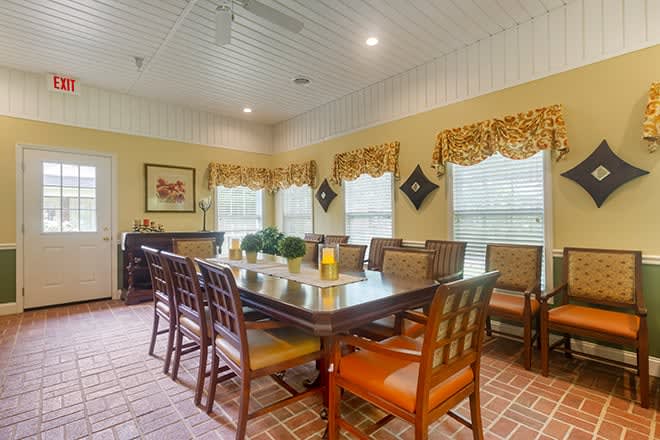 A cozy dining room with a long table, surrounded by chairs and adorned with decorative curtains and lighting.
