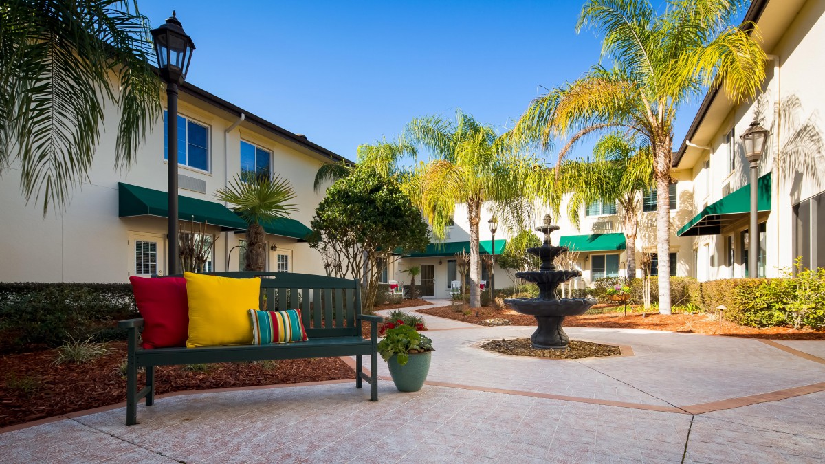 A serene courtyard featuring a central fountain surrounded by palm trees and a seating area.