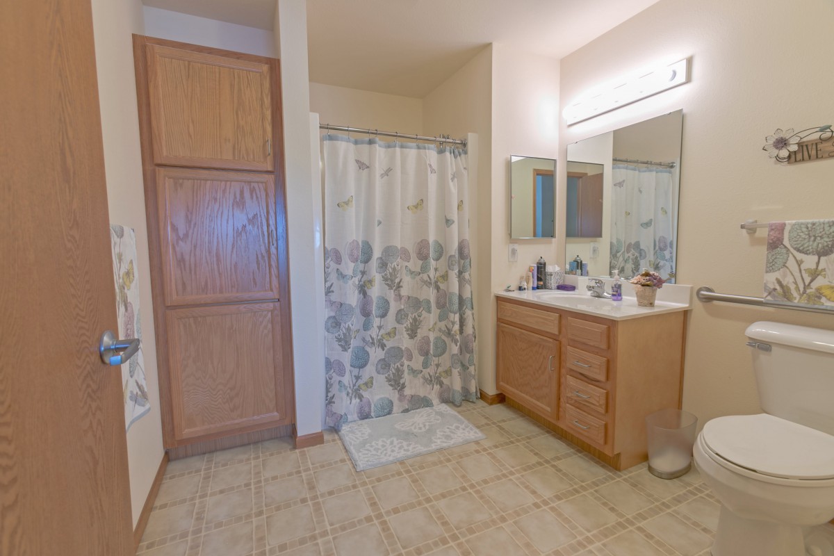 A spacious bathroom with a shower curtain, vanity, and tile flooring.