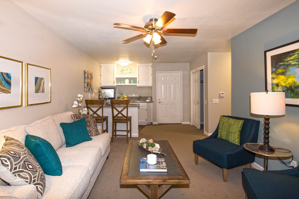 A cozy living room with modern decor, featuring a couch, coffee table, and a ceiling fan.