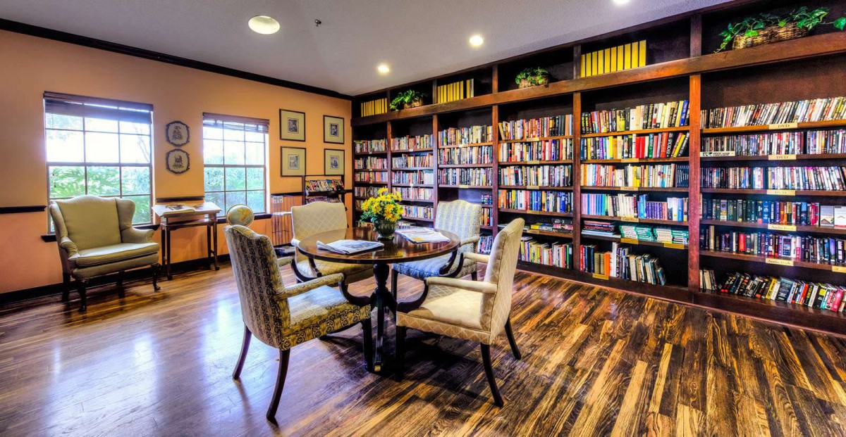 A cozy library with bookshelves filled with books, featuring a round table and chairs.