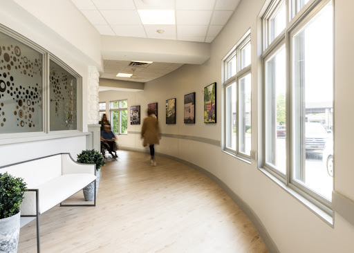 A modern and well-lit hallway in a healthcare facility, featuring large windows and artwork on the walls.