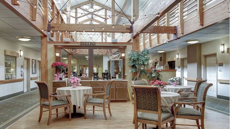 A bright and airy dining area with tables and chairs, decorated with plants and illuminated by a large skylight.