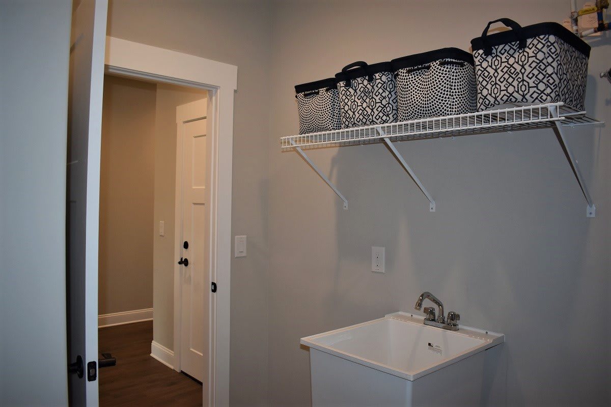 A neatly organized laundry room with storage baskets on a shelf above a utility sink.