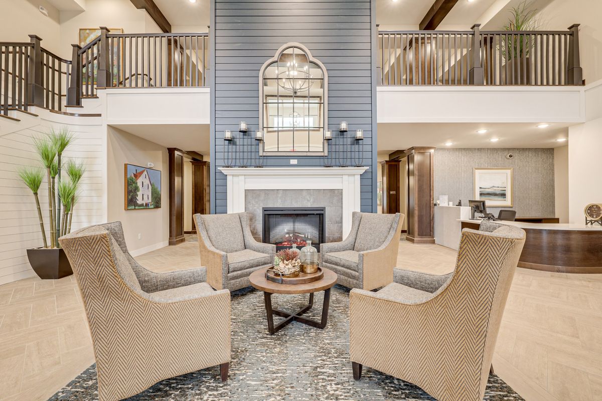A modern living room with a central fireplace, surrounded by four upholstered chairs and decorated with a large mirror above the mantle.