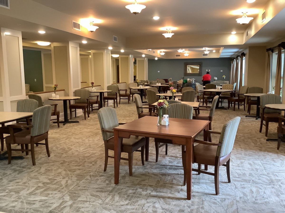 A spacious dining room with neatly arranged tables and chairs, illuminated by ceiling lights.