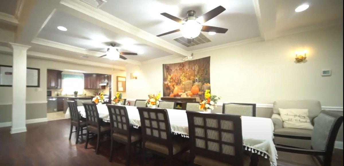 A spacious dining room featuring a long table set with decorative items and surrounded by chairs, under the glow of ceiling fans and wall art.