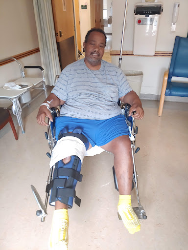 A patient sitting in a wheelchair with a knee brace, recovering in a hospital setting.