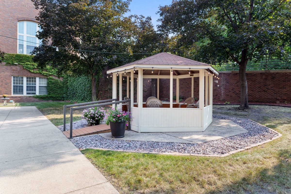 A charming gazebo surrounded by a manicured garden with a stone pathway leading up to it.