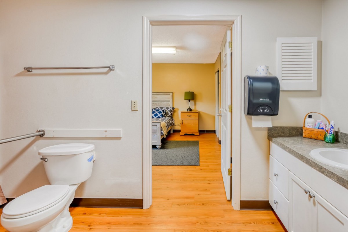 A view from a bathroom into a healthcare facility room with a bed.
