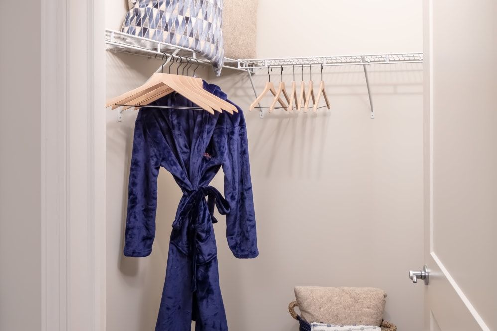 A closet with a blue robe hanging on a rack alongside empty hangers and shelves for storage.