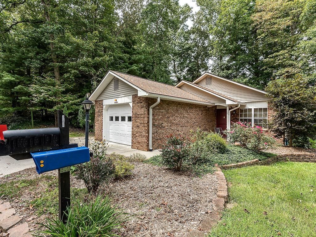 A suburban brick house with a garage, surrounded by trees and landscaping.