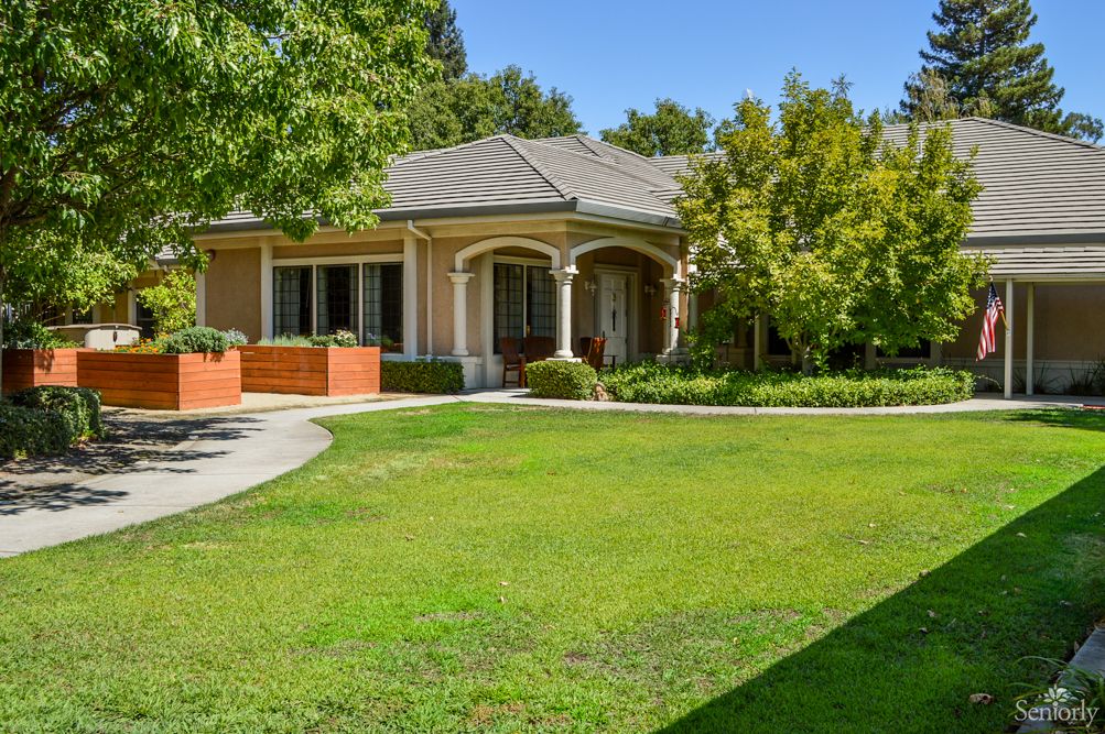 A charming single-story house surrounded by a well-maintained yard with lush greenery and trees.