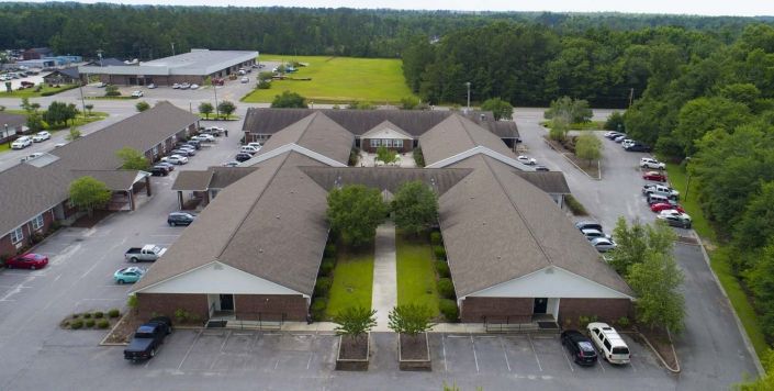 Aerial view of a complex with multiple buildings and a parking lot, surrounded by greenery.