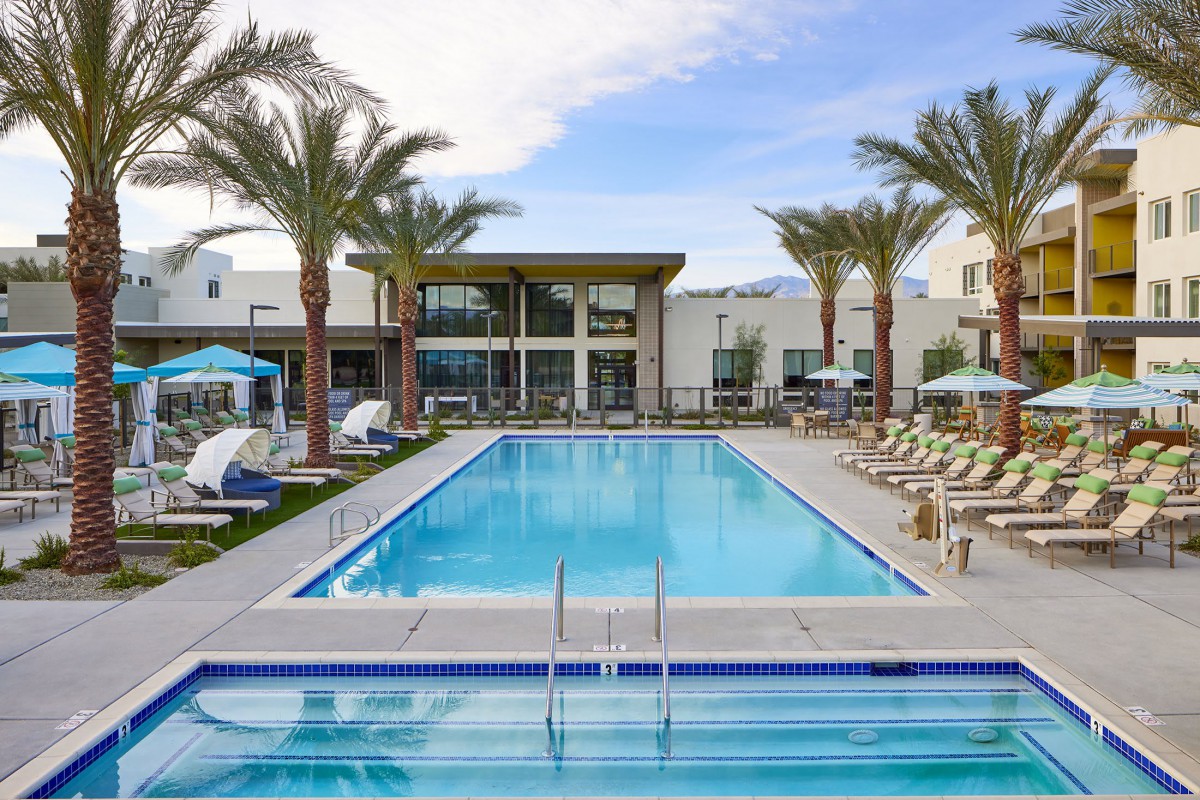A luxurious outdoor swimming pool surrounded by sun loungers and palm trees at a modern resort.