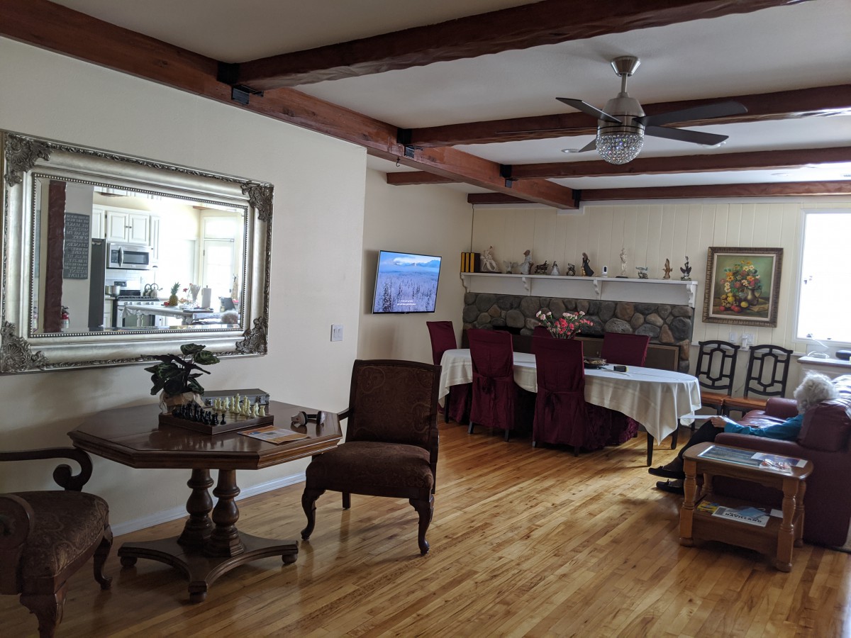A cozy living and dining area with wooden flooring, decorative ceiling beams, and a large mirror.