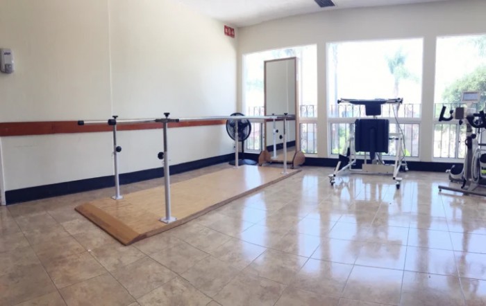 A spacious ballet studio with a wooden floor, mirrors, and ballet barres, illuminated by natural light from large windows.