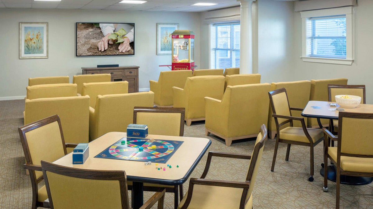 A cozy living room with yellow chairs, a game table, a large television, and a popcorn machine.