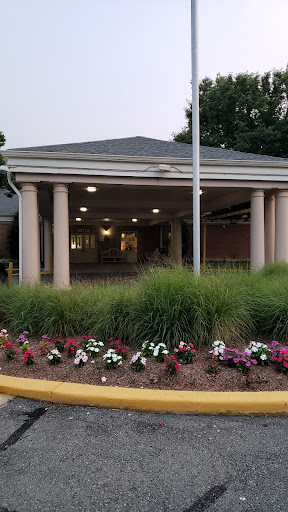 The entrance of a building surrounded by well-maintained flower beds and greenery, with columns and a flagpole.