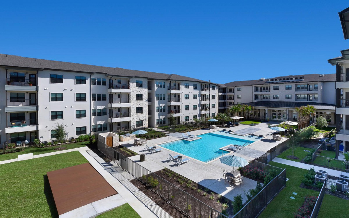 An aerial view of a modern apartment complex featuring a central swimming pool and landscaped outdoor areas.