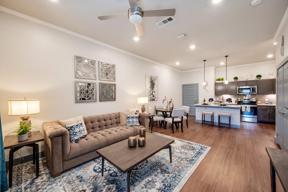 A modern open-concept living room and kitchen with stylish decor, featuring a comfortable sofa, coffee table, dining area, and contemporary lighting.