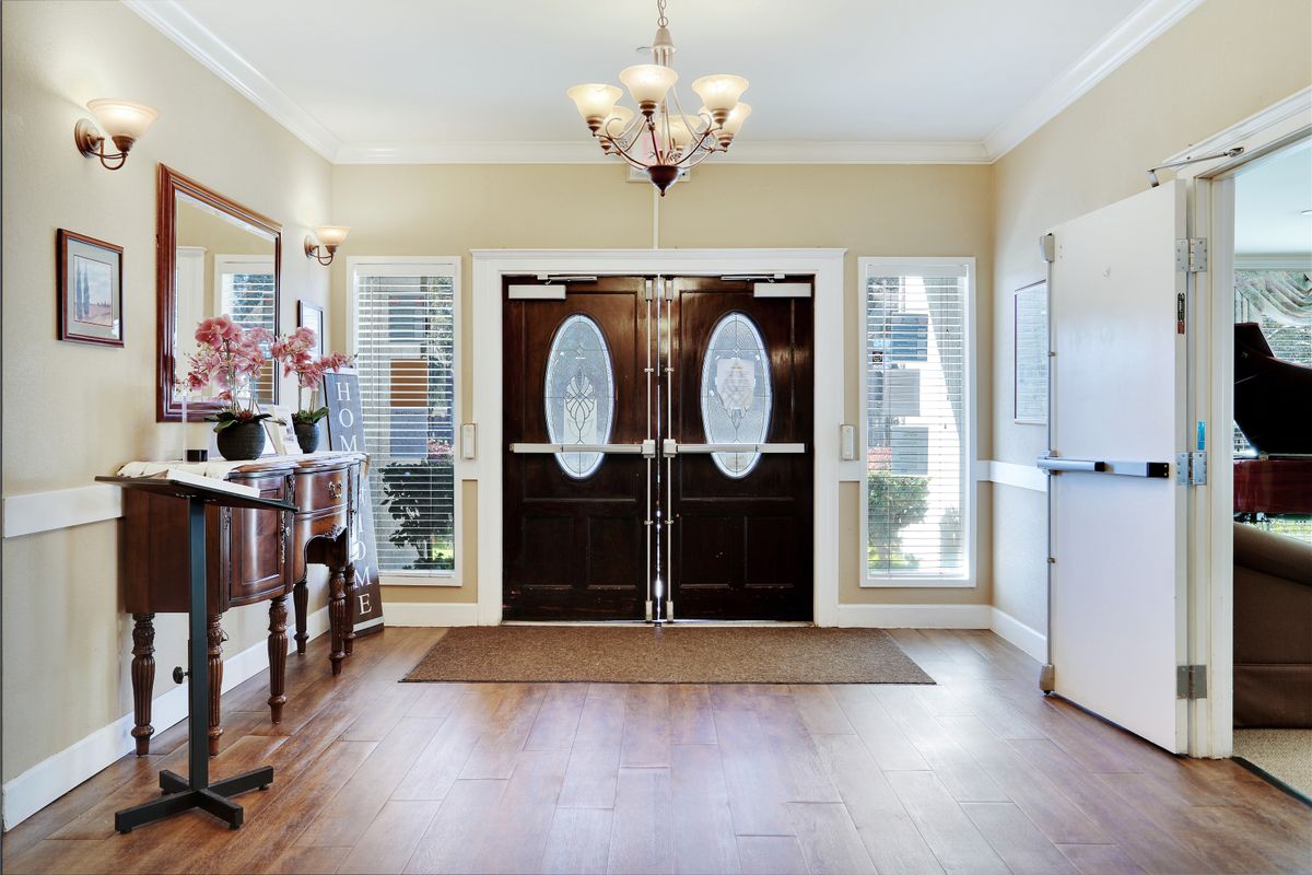 A well-lit foyer with double doors, windows, and a chandelier overhead.