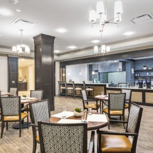 A modern restaurant dining area with neatly arranged tables and chairs, featuring elegant chandeliers and a bar counter in the background.