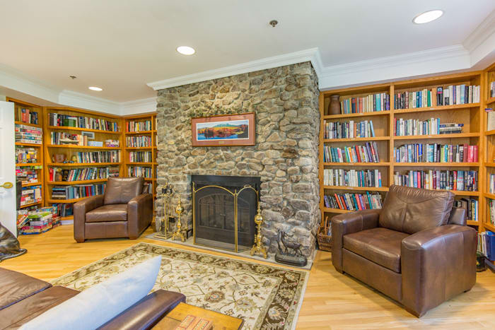 Cozy library room with a stone fireplace and surrounding bookshelves.
