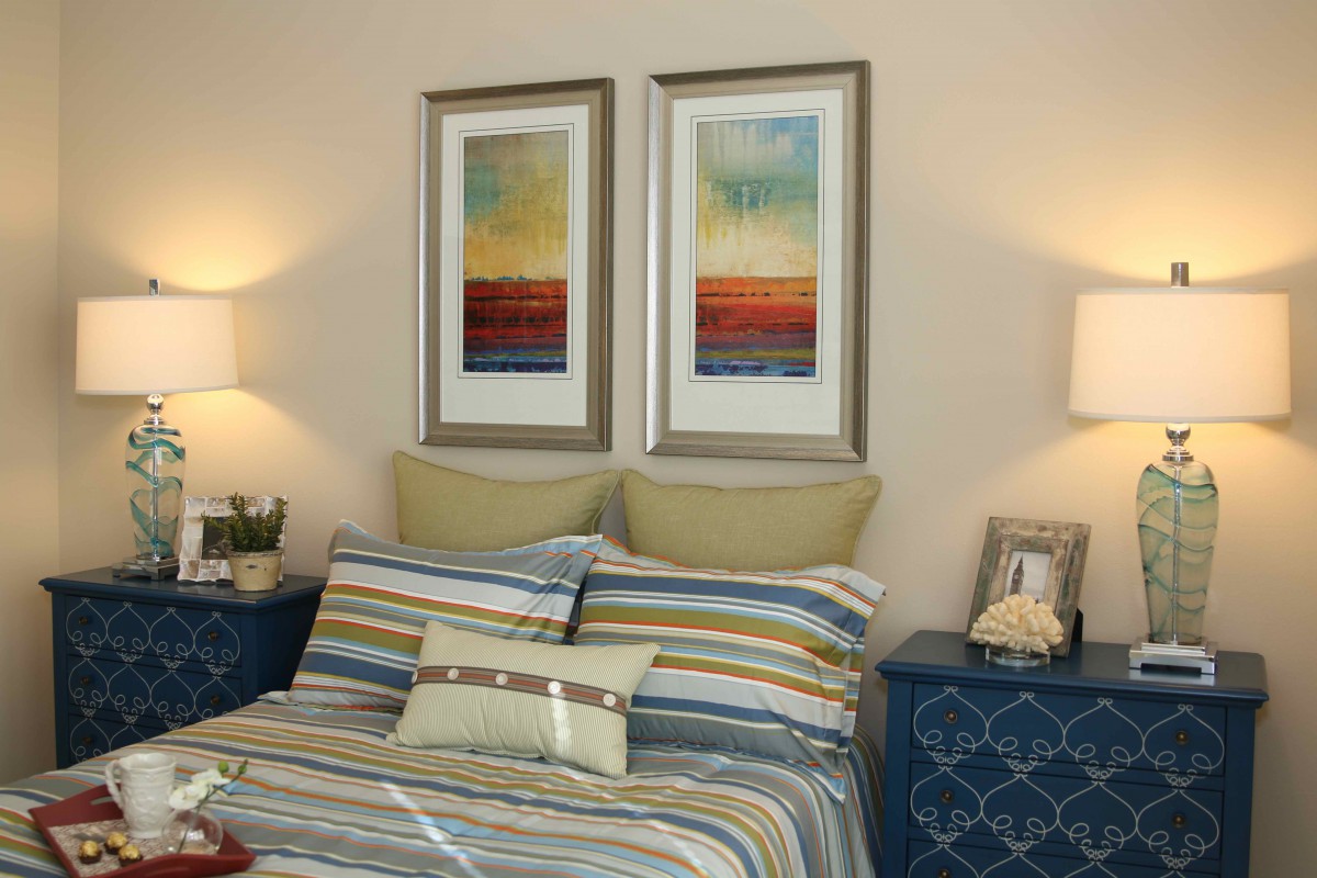 A cozy bedroom with striped bedding, framed wall art, and elegant lighting.