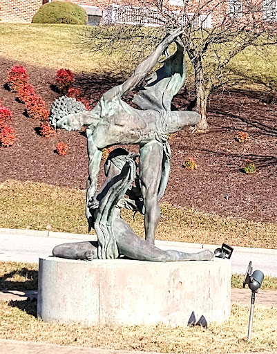 A striking bronze sculpture representing human figures in dynamic poses, set against a backdrop of autumn foliage.