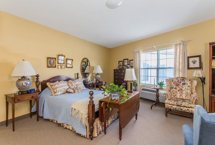 A cozy, traditionally styled bedroom featuring a wooden bed, floral decor, and natural lighting.