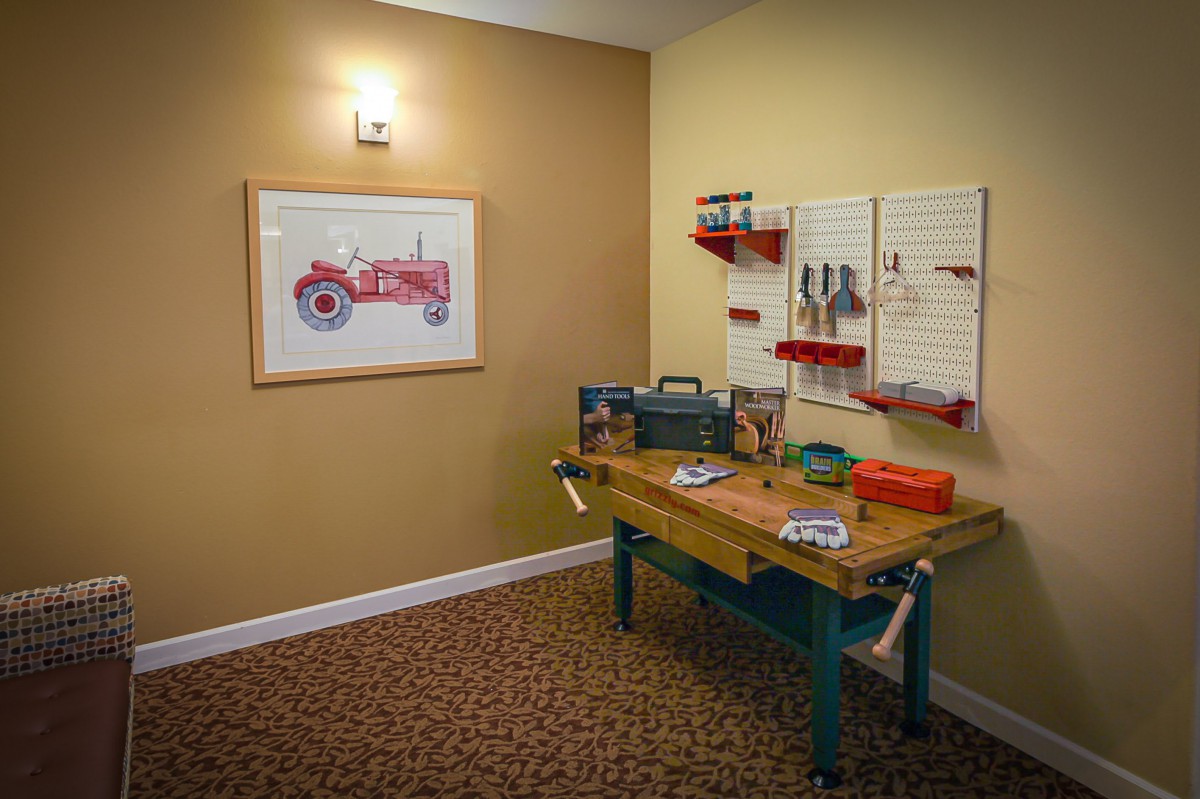 A neatly organized workshop area with a wooden workbench, various tools, and wall art of a tractor.