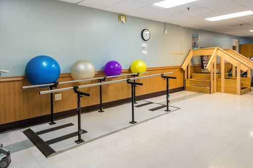A well-equipped physical therapy room featuring colorful balance balls and a barre for exercises.