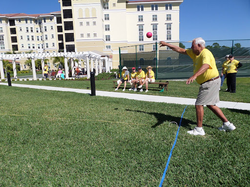 A senior man participating in an outdoor throwing event, while fellow participants watch from a bench.