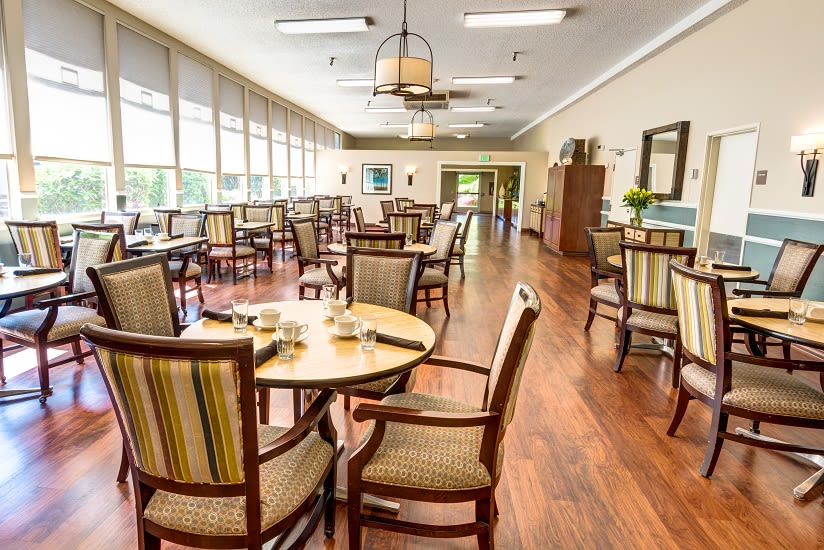 A spacious and well-lit dining area with wooden floors and neatly arranged tables and chairs.