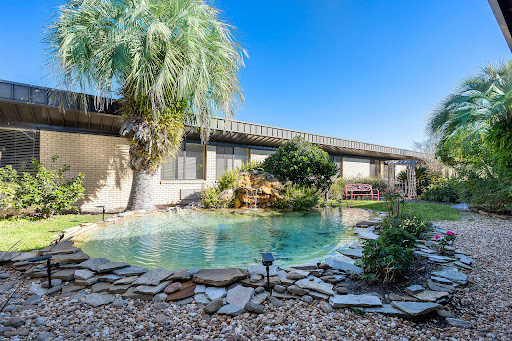 A serene view of a residential pool surrounded by lush greenery and sunny skies.