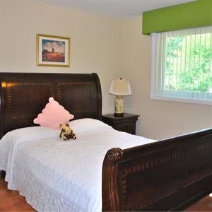 A cozy bedroom featuring a wooden bed with white bedding, a bedside lamp, and a window with green valance.