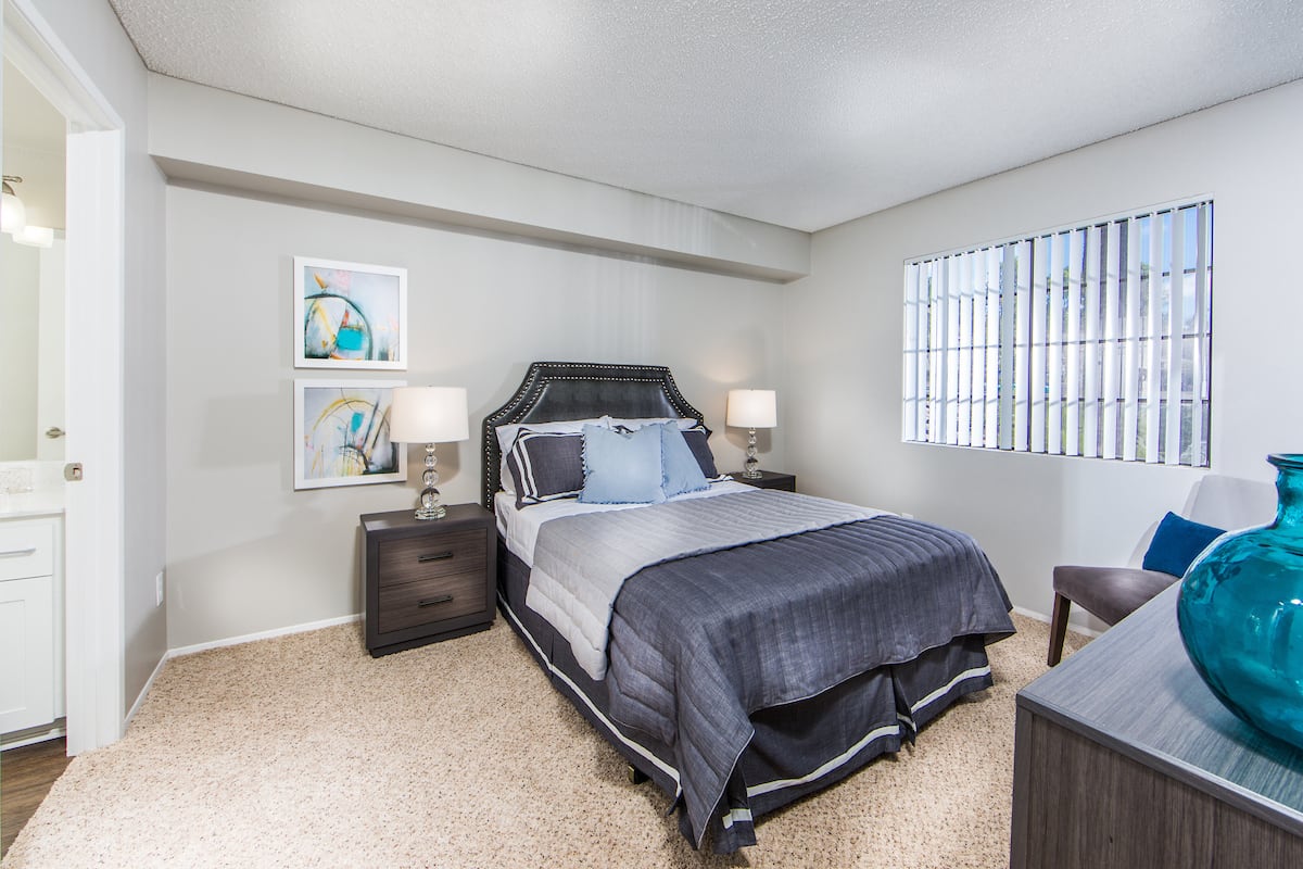 A modern bedroom featuring a neatly made bed with dark bedding, accompanied by two nightstands and soft lighting.