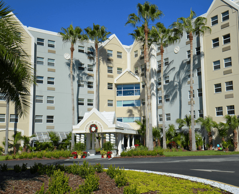 A hotel with palm trees lining the entrance on a sunny day.