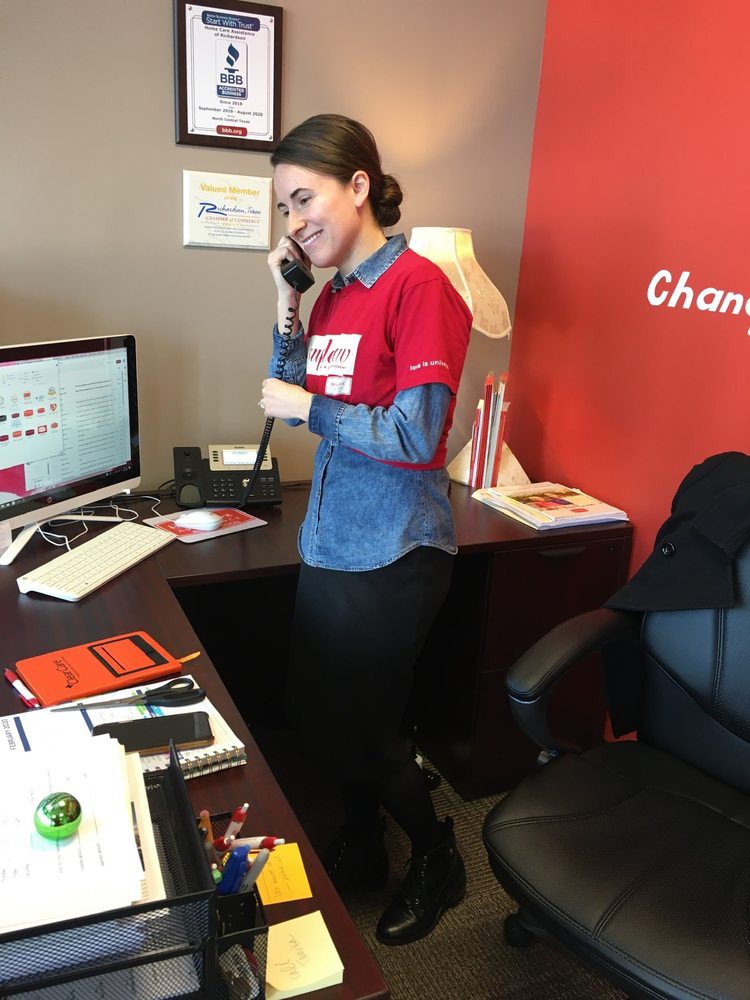 A woman is on the phone in an office setting, standing by a desk with a computer.