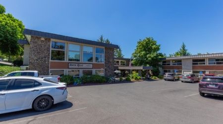 A two-story building with a parking lot and trees on a sunny day.