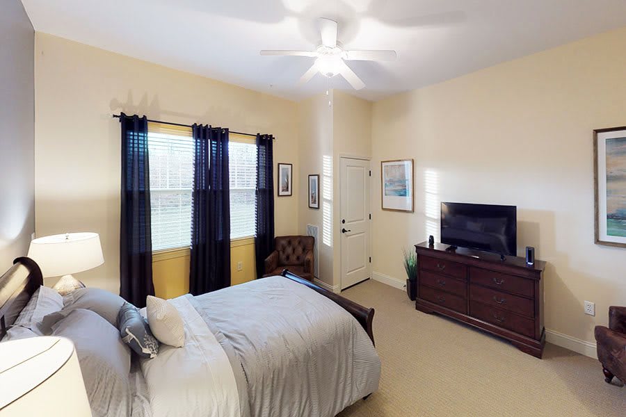 A cozy bedroom with a bed, dresser with a television, and curtains covering the windows.