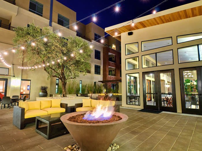 A cozy outdoor patio area with a fire pit, surrounded by comfortable seating and illuminated by string lights.