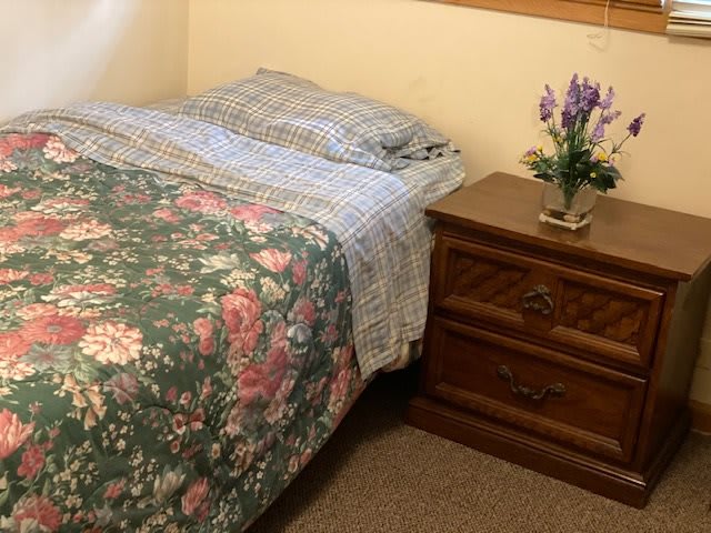 A cozy bedroom with a floral-patterned bedspread and a wooden nightstand adorned with a vase of flowers.