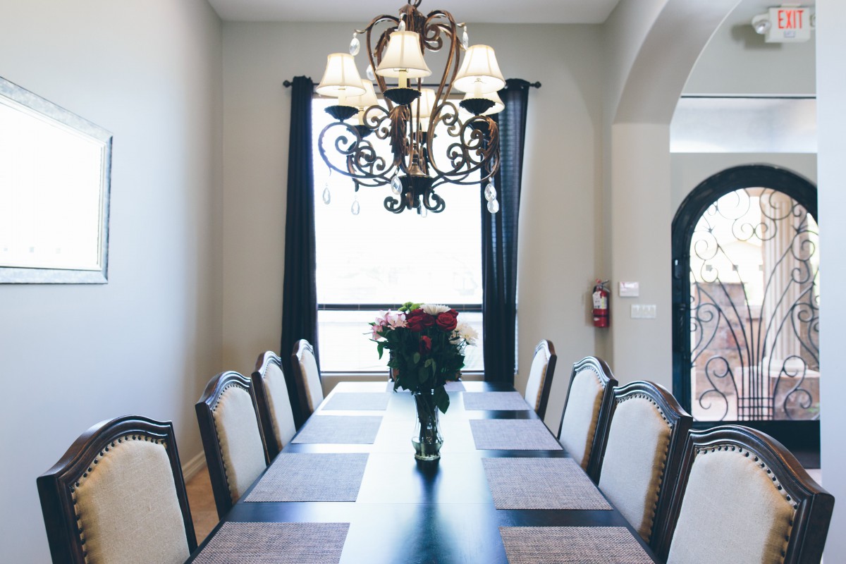 A well-decorated dining room featuring a long table with chairs, a chandelier overhead, and a vase of flowers as the centerpiece.