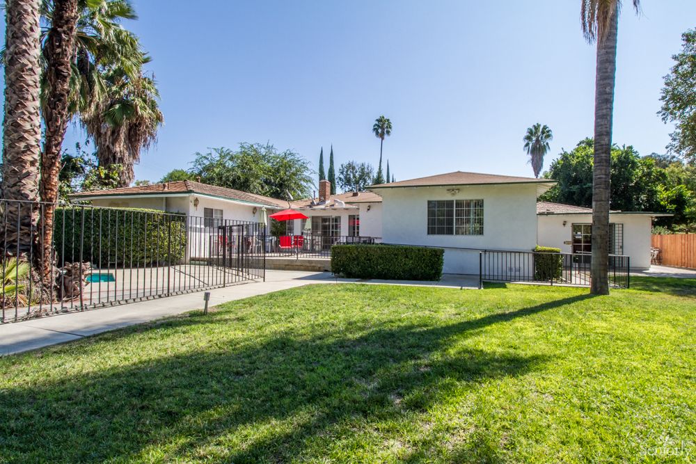 A sunny day view of a residential house with a well-maintained lawn and palm trees.