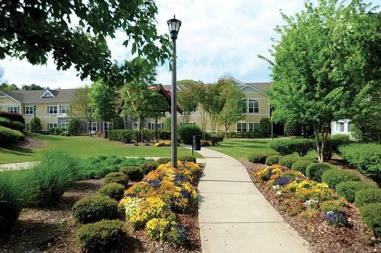 A beautifully landscaped garden path leading to a building, lined with colorful flowers and trees.