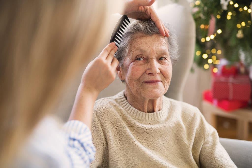 A caregiver combs the hair of an elderly woman, providing home care and comfort.